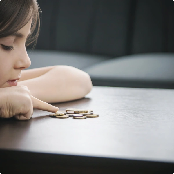 Niña pensativa contando monedas sobre una mesa