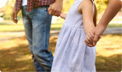 Adulto y niña tomados de la mano en un parque