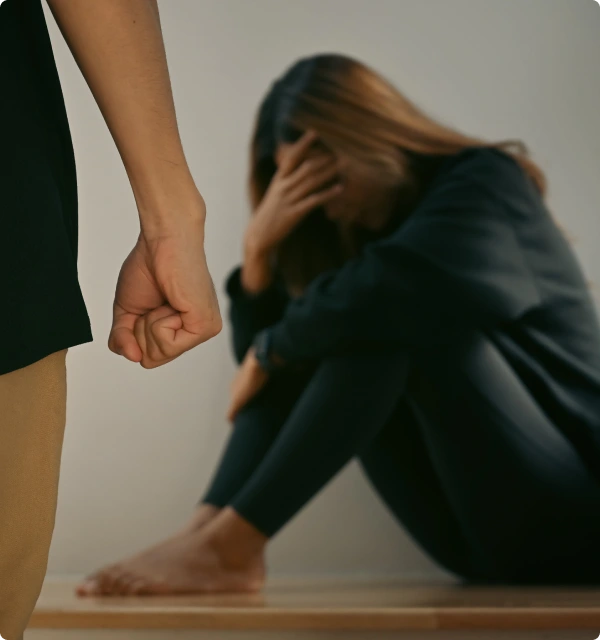 Mujer abatida sentada en el suelo junto a una persona de pie con el puño cerrado