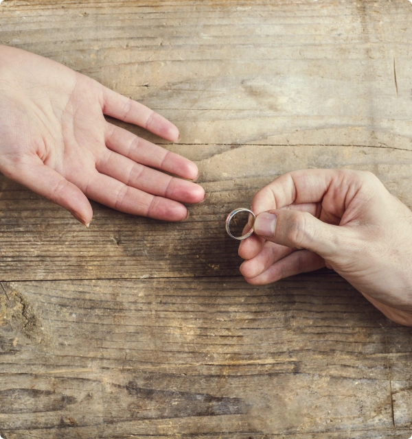 Manos de dos personas con un anillo de bodas sobre una mesa de madera