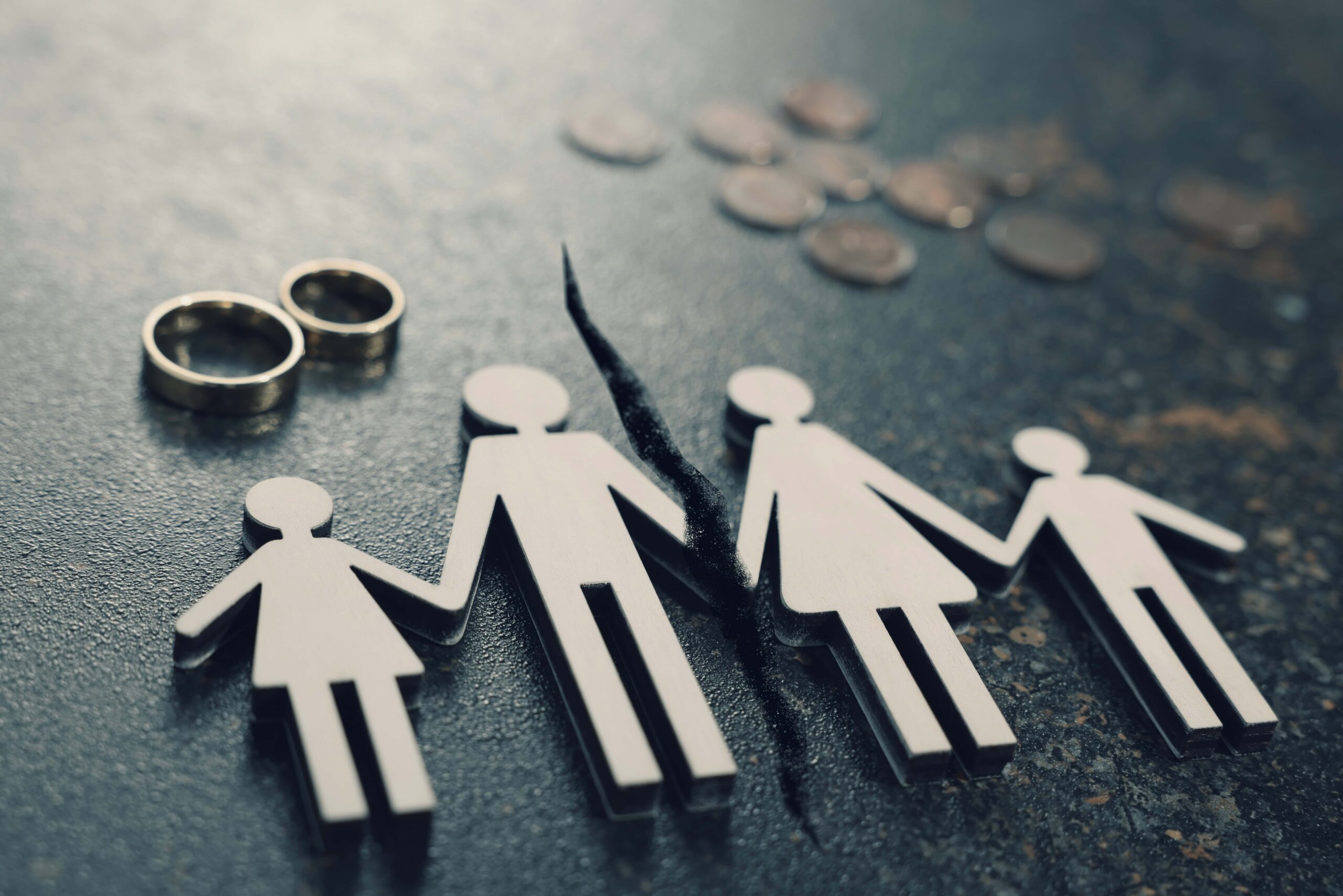 Figuras de papel de una familia separada junto a anillos y monedas